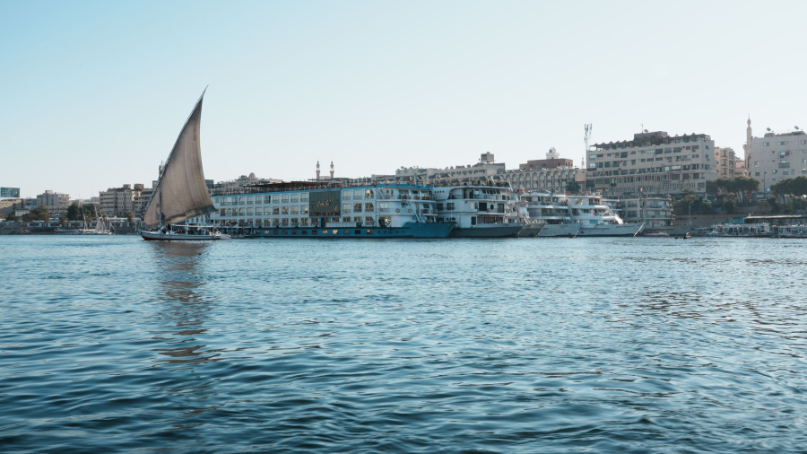 A river cruise ship sails along the Nile River near ancient Egyptian temple ruins.