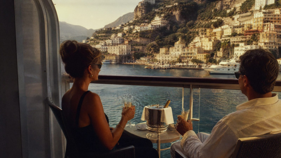 Couple enjoying champagne on a cruise ship balcony as the ship arrives in a Mediterranean harbour town