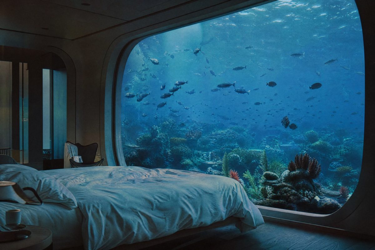 Underwater hotel bedroom with a window looking into a coral reef full of fish