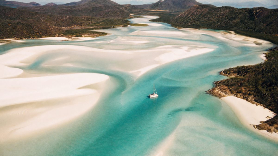 Aerial view of white silica sand and turquoise water at a Whitsundays inlet with a sailing catamaran